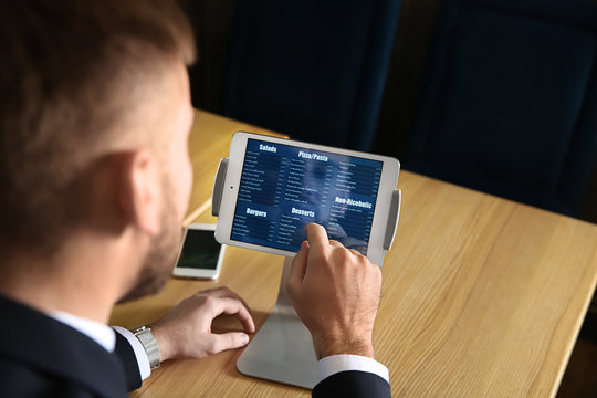 Young man with tablet PC looking through menu in restaurant