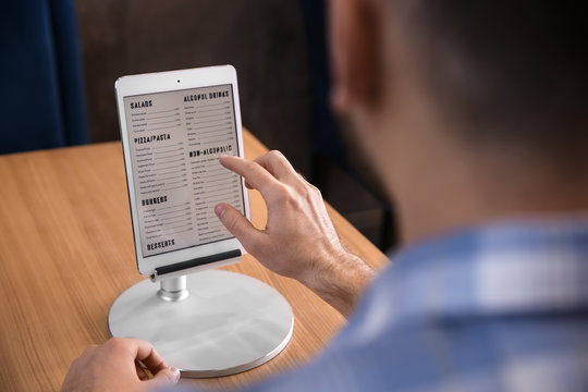 Young Man With Tablet PC Looking Through Menu In Restaurant