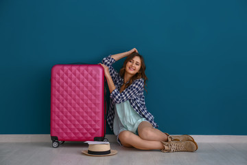 Female tourist with luggage sitting near color wall