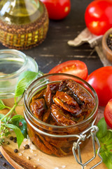 Sun dried tomatoes with olive oil in a jar on black stone or concrete table.