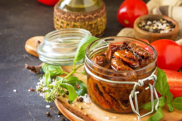 Sun dried tomatoes with olive oil in a jar on black stone or concrete table. Copy space.