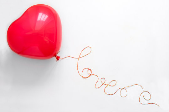 Creative concept. Hand holding red heart shape balloon with Love word from thread on white wooden background. Flat lay. Top view. Valentines day celebration