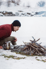 Tourist is making campfire surrounded by snow near of the frozen lake. Concept adventure active...