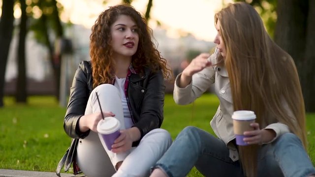Two beautiful young women talking and drinking coffee outdoors. Communication and gossip.