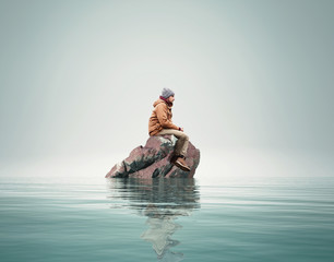 Man stands on a rock in the middle of a lake.
