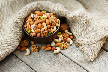 Wooden bowl with nuts on a wooden background, near a bag from burlap.
