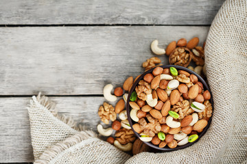 Wooden bowl with nuts on a wooden background, near a bag from burlap.