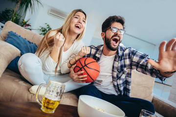 Couple is watching basketball game on the sofa at home.