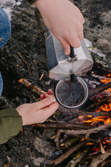 Traveling-woman  a  sits near camp fire an in winter time and pours itself hot coffee . Concept adventure active vacations outdoor. Winter camping