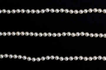 Rows of pearl necklace on the black background. Elegance and jewelry concept. Top view, flat lay, copy space, card layout