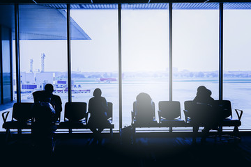 Silhouettes of business people traveling on airport; waiting at the plane boarding gates.