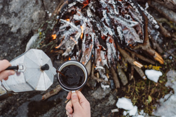 Traveling-woman  a  sits near camp fire an in winter time and pours itself hot coffee . Concept adventure active vacations outdoor. Winter camping