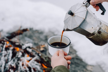 Traveling-woman  a  sits near camp fire an in winter time and pours itself hot coffee . Concept adventure active vacations outdoor. Winter camping