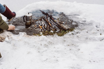 Traveling girl sits near camp fire with a cup of hot coffee an in winter time. Concept adventure active vacations outdoor. Winter camping