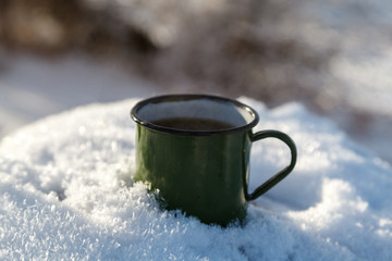 Drinking tea in the winter outdoors. Mug of hot tea in the snow, morning tea outdoors in the rays of the winter sun.