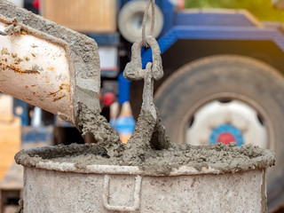Concrete mixer truck pouring liquid concrete into the tower crane bucket at the construction site