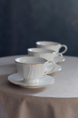Tableware for tea party - three cups - on white tablecloth on dark gray background. Close-up, copy space