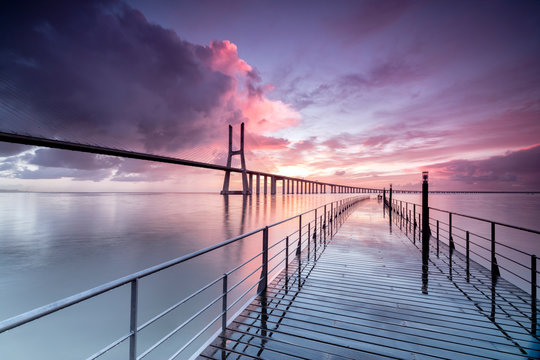 Fototapeta Sunrise colors the clouds reflected in Tagus River and frame the Vasco da Gama bridge in Lisbon Portugal Europe