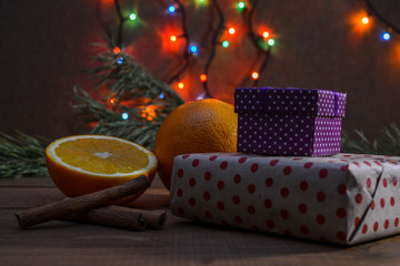 Beautiful festive picture. Oranges, cinnamon, gift boxes, Christmas tree and Christmas lights (luminous garland).