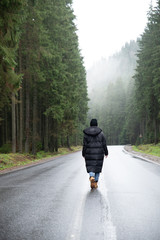 young woman standing at the middle of the road in winter mountains forest