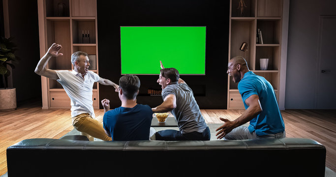 A group of students is watching a TV and celebrating some joyful sports moment, sitting on the couch in the living room.