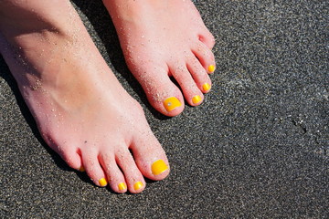 Pair of bare feet with yellow nail polish and a toe crystal at the beach