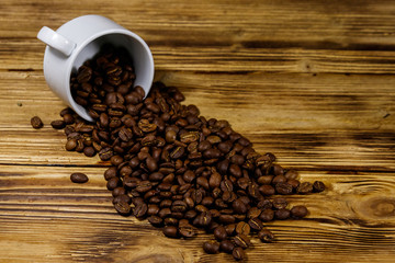 Roasted coffee beans spill out of cup on wooden table