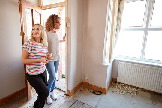 Excited Female Couple Opening Front Door Of New Home
