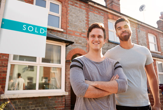 Portrait Of Two Men Standing Outside New Home With Sold Sign