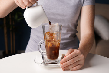 Woman making tasty frappe coffee at table