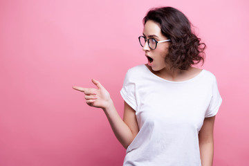 Fototapeta Good looking young Caucasian woman in round transparent eyewear, keeps hand raised, dressed in casual outfit, pretends holding something wonderful, isolated over pink background. Look there obraz