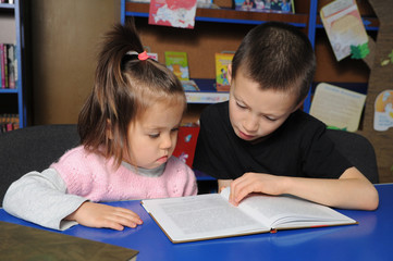 Children in library reading interesting book. Little girl and boy together learning