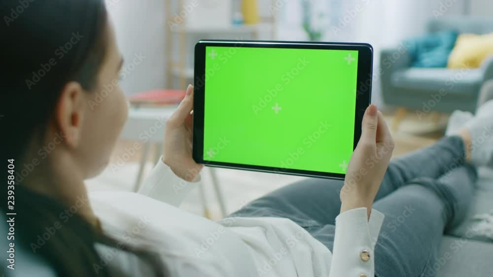 Poster young woman at home resting on a couch using with green mock-up screen tablet computer in horizontal