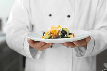 Male chef with tasty salad in kitchen, closeup