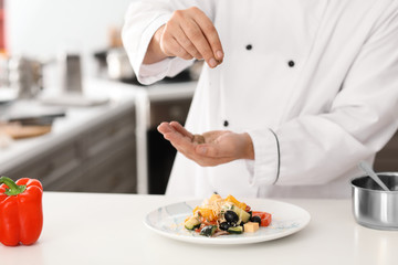 Obraz na płótnie Canvas Male chef adding spices to tasty salad in kitchen, closeup
