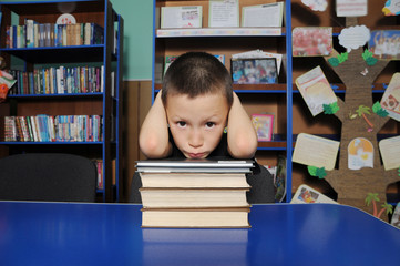 Boy sitting in library, putting head on pile of books