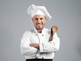 Male chef with kitchen utensils on grey background