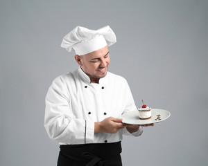Male chef with tasty dessert on grey background