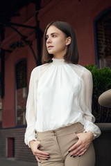 Female fashion concept. Outdoor waist up portrait of young beautiful woman posing on old street. Model wearing stylish clothes, looking at camera. Sunny day. City lifestyle. Copy, empty space for text