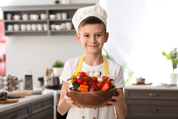 Cute little chef with vegetables in kitchen