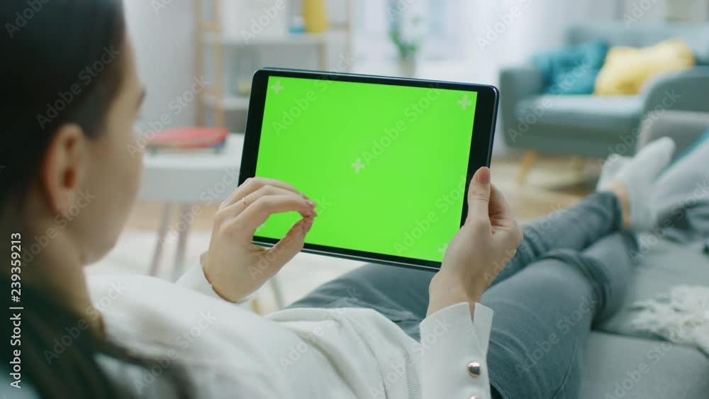 Poster young woman at home resting on a couch using with green mock-up screen tablet computer in horizontal