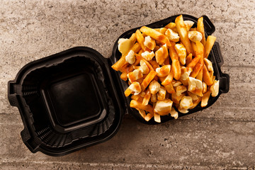 Poutine in a takeout container. Cooked with french fries, beef gravy and curd cheese. Canadian...