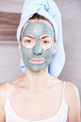Woman applying mask moisturizing skin cream on face looking in bathroom mirror. Girl taking care of her complexion layering moisturizer. Skincare spa treatment.