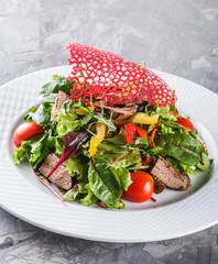 Fresh green salad with lettuce, arugula, sweet pepper, tomatoes and beef in plate over dark table. Healthy food, dieting