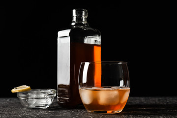 Glass and bottle of cold whiskey on dark background