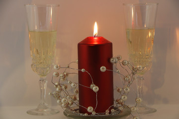 Two glasses of champagne, a red candle, a wreath on a white background.
