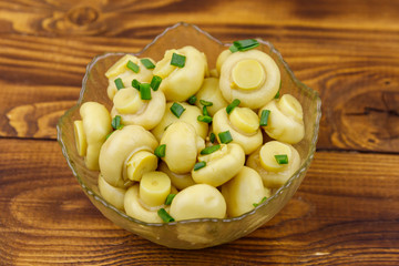 Glass bowl with pickled champignons. Marinated mushrooms on wooden table