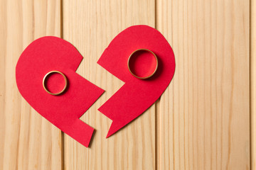 Broken red heart with rings on wooden background. Concept of divorce
