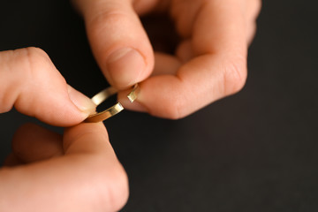 Female hands with broken ring on dark background, closeup. Concept of divorce