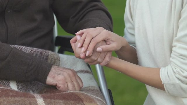 Daughter stroking hand of disabled father, supporting during treatment period